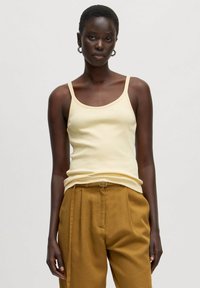 Geel geribbelde tanktop met dunne bandjes, gecombineerd met hoog getailleerde, bruine textuurbroeken. Eenvoudig ontwerp, geen patronen of accenten.