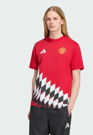 Ung person med langt blond hår iført en rød Manchester United-trøje med sort-hvid ternet design og sorte bukser med Adidas-logo.