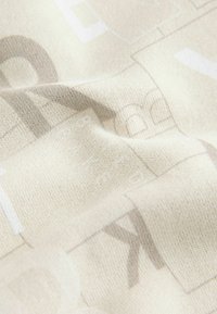 Jasno-beżowy materiał o teksturowanej powierzchni, z delikatnym, monochromatycznym wzorem liter i kształtów. Miękki, elastyczny materiał.