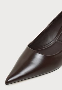 Gros plan d'une chaussure plate en cuir marron foncé à bout pointu, montrant une texture lisse et un intérieur rembourré.