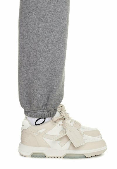 Sneakers bianche con pannelli testurizzati e accenti grigio chiaro, abbinate a pantaloni jogger grigi con polsini elasticizzati e calzini neri e bianchi con motivo a fantasia.