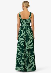 Robe maxi en tissu vert foncé avec un motif de feuilles vert clair. Bretelles larges, dos smocké et silhouette fluide.