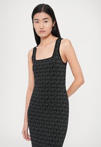 Čierne pletené šaty s hranatým výstrihom, ramienkami typu tank top a celoplošným vzorom MK v tmavšom odtieni, vytvárajúc jemný textúrovaný vzhľad.