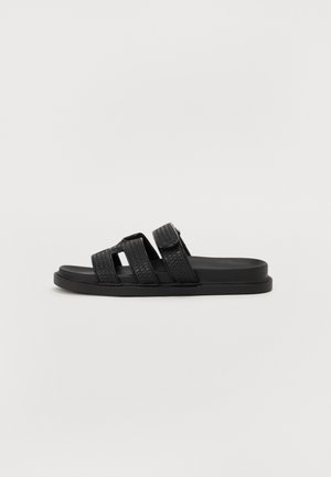Sandalias negras tipo slide con tres correas entrelazadas, suela plana y acabado texturizado. Diseño sencillo adecuado para uso casual.