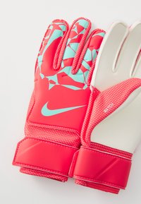 Röda målvaktshandskar med ett geometriskt mönster i ljusblått, texturerat grepp och elastiskt handledsband. Nike-logotypen syns tydligt.