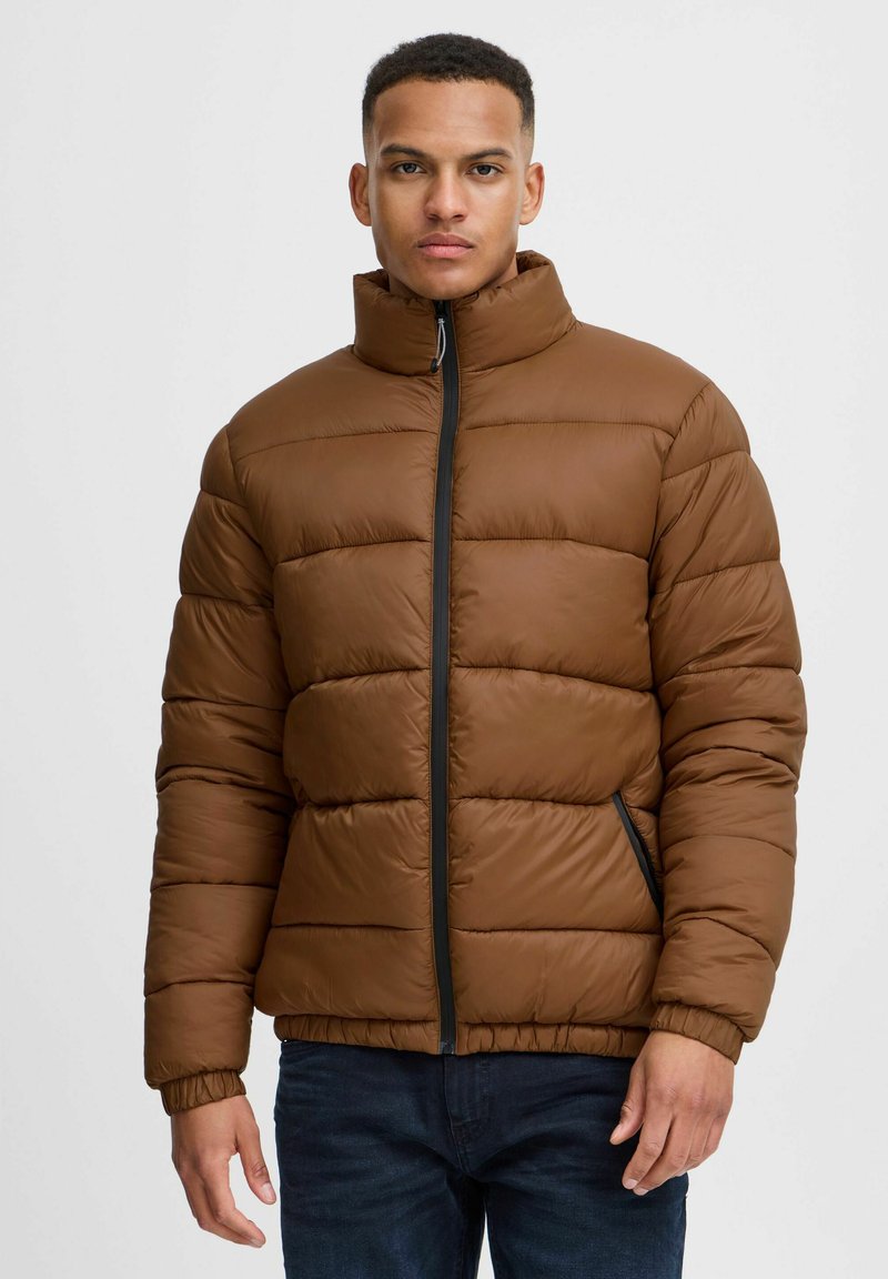 Brun puffer-jakke med boksformet quiltedesign, høy krage og svart glidelåsdetaljering. Har elastiske mansjetter og sidelommer.