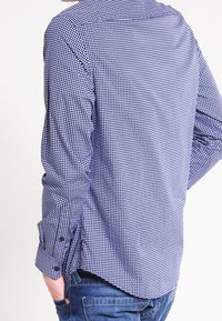 Långärmad blå och vit rutiga skjorta med knappmanschetter, krage och rundad nederkant, gjord av lättviktsmaterial.