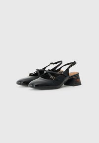 Schwarze Lackleder-Slingback-Schuhe mit einem Kreuzbanddesign, ausgestattet mit einem niedrigen Blockabsatz und einem strukturierten Absatzakzent.