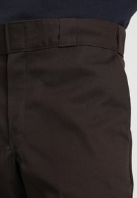 Pantalones de algodón marrones con una textura suave, frente plano y una cinturilla estándar con trabillas para cinturón. Sin patrones ni piezas metálicas visibles.