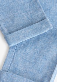 Világoskék farmeranyag összehajtott szegéllyel, közelről mutatva a szövet textúráját és varrását, fehér háttér előtt.