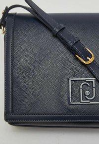Borsa a tracolla in ecopelle blu navy con superficie testurizzata, tracolla regolabile e applicazioni in metallo dorato con dettaglio del logo.