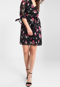 Svart blommig klänning med rosa och vita blommor, genomskinliga ärmar, midjeband, ovanför knä längd, ihop med svarta ankelsandaler.