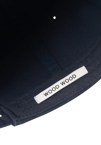 Innenraum eines dunkel marineblauen Stoffhuts mit einem weißen rechteckigen Etikett, auf dem "WOOD WOOD" in schwarzen Buchstaben aufgenäht ist.