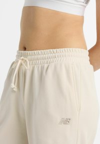 Pantalon de survêtement couleur crème avec une ceinture élastique, un cordon de serrage ajustable et des poches latérales. Présente un logo brodé discret.