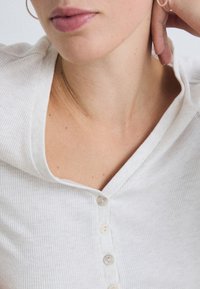Vitribbad topp i vitt med V-ringning och sex tygklädda knappar fram. Mjuk textur med synliga sömdetaljer.