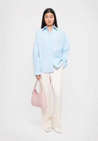 Camicia azzurra chiara con vestibilità comoda, abbinata a pantaloni bianchi a gamba larga e a una borsa a spalla in pelle rosa. Texture lisce in tutto il look.