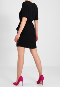 Svart kortärmad klänning med bälte i midjan, med rak skärning och slät textur. Matchad med ljusrosa högklackade skor.