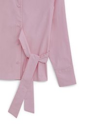 Camicia rosa chiaro con maniche lunghe, chiusura a bottoni e dettaglio con nodo laterale. Il materiale è liscio con una leggera lucentezza.