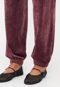 Velvet mauve sweatpants met elastische boorden, gecombineerd met zwarte ballerina's met een doorzichtige neu en een dunne band over de voet.