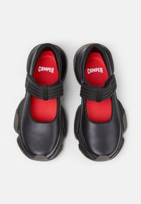 Scarpe di pelle nera con soletta rossa e cinturini elasticizzati; suole in gomma con una forma e una texture uniche per aderenza e supporto.