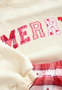 Beez riidest sviiter, millel on mitmevärviline "MERRY" kirjastiil koos lille- ja triibumustritega. Punased pliiatsipüksid, millel on elastne vöökoht.