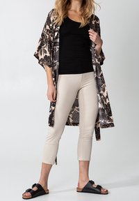 Lång blommig kimono i svart och beige över en figurnära svart topp, kombinerad med krämfärgade cropped byxor och svarta sandaler med spänne.