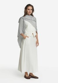 Hvid lang nederdel og tætsiddende hvid top, lagdelt med et gråt og hvidt stribet sjal. Brune vævede flade sko fuldender outfittet.
