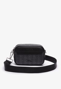 Borsa a tracolla nera Lacoste con motivo geometrico, logo impresso, ganci argentati e tracolla larga regolabile su sfondo bianco.