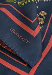 Marineblauwe zijden sjaal met rode geometrische randen, bloemmotieven en het "GANT" logo geborduurd in rode draad.