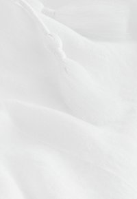 Weißer Stoff mit weichem, strukturiertem Leinen und zwei dekorativen weißen Quasten, die dem Gesamtdesign Kontrast und Detail verleihen.