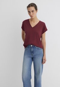 Burgundy V-neck t-shirt with short sleeves, relaxed fit, paired with high-waisted light blue jeans featuring a classic five-pocket design.