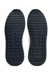 Zwarte rubberen sneakerzolen met een gestructureerd oppervlak. Opvallende ribbels en patronen zorgen voor grip, met een geprint logo aan de onderkant.