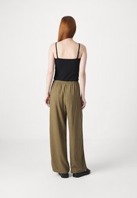 Zwarte mouwloze top met dunne banden, gecombineerd met losse, olijfgroene wijde broek van lichtgewicht stof. Zwarte platte sandaal.