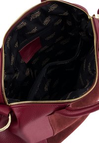 Kožená kabelka barvy burgundské s hladkým povrchem. Vnitřek je vybaven černou látkovou podšívkou s logem, kapsou na zip a organizačními přihrádkami.