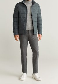 Chaqueta de plumas gris oscuro con secciones acolchadas horizontales, combinada con un suéter gris claro, pantalones grises y zapatillas blancas.