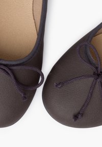 Bailarinas en material sintético marrón oscuro con un acabado suave, que presentan una puntera redondeada y un lazo de cinta morado en la parte delantera.