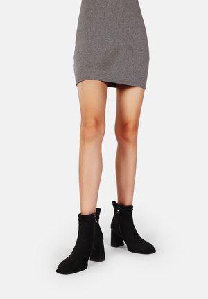 Stivaletti neri in suede con tacco a blocco, dotati di chiusura con zip e design con risvolto. Texture liscia e silhouette elegante.