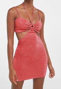 Punainen, kimalteleva minisatiini, jossa on leikattu sivuosat, ohuet hihnat ja solmittu keskityksellinen yksityiskohta, jossa on pyöreä aksentti. Muotoiltu siluetti.