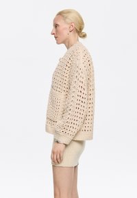 Maglione beige a maglia aperta con una vestibilità ampia, polsini e orlo a coste spessi, abbinato a una mini gonna di maglia color crema. Tessitura testurizzata in tutto il capo.