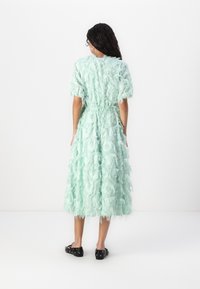 Mint green dress with ruffled texture, short sleeves, and a cinched waist. Falls mid-calf, with fringed hem and side pockets. Black shoes.
