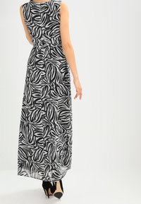 Robe maxi en noir et blanc avec un motif de feuilles, design sans manches, taille cintrée et jupe fluide, associée à des escarpins noirs.