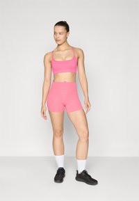 Soutien-gorge de sport rose vif et short taille haute assorti. Tissu lisse et extensible avec des coutures minimes. Chaussures de sport noires et chaussettes blanches.