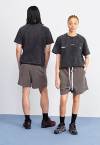 Mørkegrå bomullsblandede t-skjorter med korte ermer, kombinert med matchende shorts med snøring. Begge antrekk har en avslappet og ledig passform.