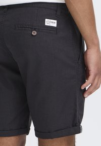 Pantalones cortos negros de tejido con una textura suave, con dobladillo enrollado, bolsillos laterales y un bolsillo trasero con una etiqueta de logo y botón.