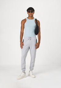 Light blue tank top, gray sweatpants with zippered pockets, and white sneakers. Accessories include black fanny pack and sunglasses.