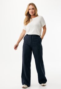 Biały top z krótkim rękawem w połączeniu z granatowymi spodniami o szerokich nogawkach z pionowymi białymi paskami. Do stroju dołączone są jasne sneakersy.