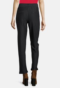 Svarta randiga byxor med skräddarsydd passform; har snedställda bakfickor och manschettnederkant. Bärs med bruna klackstövlar.