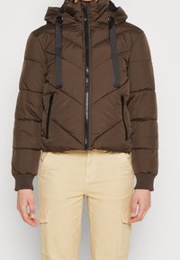 Brown puffer jacket with a hood, featuring black drawstrings, zip closure, and angled quilted pattern. Ribbed cuffs and zippered pockets.