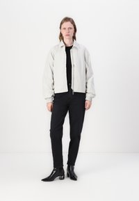 Helle graue Bomberjacke mit Reißverschluss, elastischen Bündchen und lässigem Schnitt, kombiniert mit schwarzen Jeans und spitz zulaufenden Stiefeletten mit Absatz.