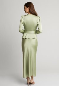 Długa, dopasowana sukienka z miękkiego, jasnobeżowego satyny z peplum w talii, bufiastymi rękawami i elegancką sylwetką. Gładka tekstura i minimalne detale.